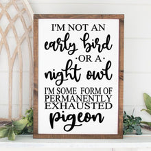 Load image into Gallery viewer, A painted wood sign with a phrase 'I'm not an early bird or a night owl, I'm some sort of permanently exhausted pigeon' written in black. The sign is displayed in a frame and set against a home background.