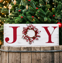 Load image into Gallery viewer, A rustic white wooden sign spelling JOY, with a red J and Y and a red-and-white striped peppermint candy wreath in the center, displayed on a wooden barrel in front of a decorated Christmas tree.