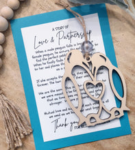 Load image into Gallery viewer, A wooden charm ornament shaped like a pair of penguins with a heart joining them together with a heartfelt card describing the dating rituals of penguins .
